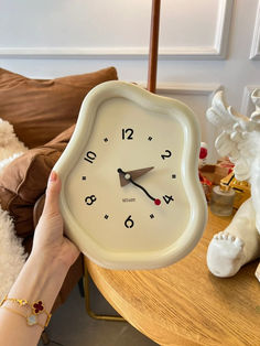 a person holding up a white clock on top of a table next to a teddy bear