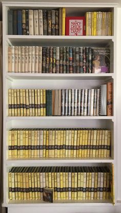 a book shelf filled with lots of books on top of white shelves next to a wall