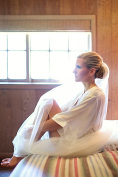 a woman sitting on top of a bed wearing a white dress and veil over her head