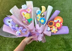 a hand holding a bunch of fake flowers on top of a grass covered field,