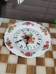 a clock with flowers painted on it sitting on a checkered floor