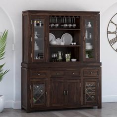 a dining room hutch with glass doors and plates on the top, in front of a clock