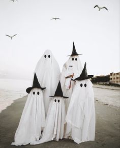 three white ghost figures standing on the beach with black hats and long cloaks over their heads