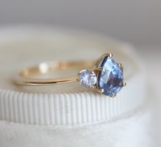 a close up of a ring on top of a white cloth covered box with an object in the background