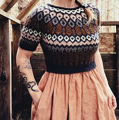 a woman standing in front of a wooden fence wearing a brown dress and black hat