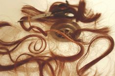 scissors and hair are laying on top of the pile of long, wavy brown hair