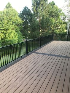 a wooden deck with black railing and trees in the background