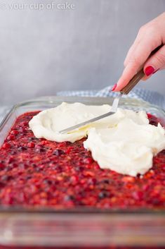 a woman is spreading cream on top of cranberry sauce in a glass dish