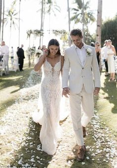 a bride and groom walking down the aisle at their wedding ceremony in hawaii, with white petals on the grass