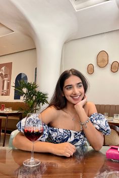 a woman sitting at a table with a glass of wine in front of her smiling