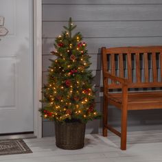 a small christmas tree in a pot next to a wooden bench on the front porch