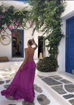 a woman in a purple dress is walking down the street with her hand on her head