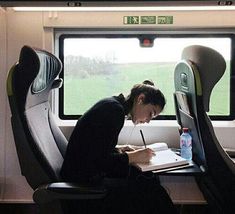 a woman writing on a paper while sitting in a seat next to an open window