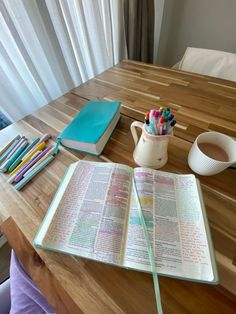 an open bible on a wooden table next to a cup of pencils and markers