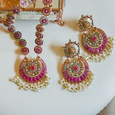 Adorn into the extravagant fusion of grace and royalty! Paint yourself in luscious shades of nauratan stones enhanced by pearl moti hanging with a classic embodiment of ravishing flower motif design radiating elegant femininity. The set includes a mala that comes with an adjustable dori and a pair of dangle earrings. Approximate mala length is and approximate earrings length is. Gold-plated on high-quality brass as base metal. Made by order. Kindly allow 4-6 weeks for the delivery of this item. Fusion Style Kundan Necklace For Navratri, Festive Fusion Kundan Necklace For Navratri, Temple Jewelry Sets With Pearl Drop For Festive Season, Temple Jewelry Sets With Pearl Drop For Festive Occasions, Traditional Temple Necklace With Pearl Drop For Festive, Festive Pearl Jhumkas, Traditional Pearl Drop Jewelry Sets For Celebration, Festive Pearl Necklace With Latkans For Wedding, Wedding Pearl Necklace With Latkans