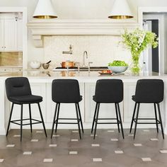 three black chairs sitting in front of a white kitchen island with marble counter tops and gold pendant lights