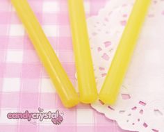 three yellow candles sitting on top of a pink and white checkered table cloth with doily