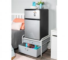 a silver refrigerator freezer sitting on top of a metal drawer next to a bed