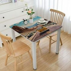 a table and chair with a painting on it in front of a white dresser next to a window