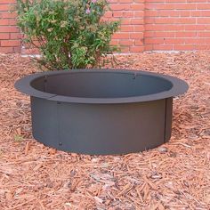 a round fire pit sitting on top of mulch next to a brick wall and tree