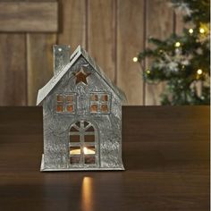 a small metal house with a lit candle in front of it on a table next to a christmas tree