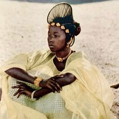 an african woman sitting on the beach with her arms crossed and wearing a yellow dress