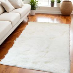 a living room with a white couch and rug on top of the wooden floor next to a window