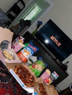 two pizzas and snacks are sitting on the floor in front of a television