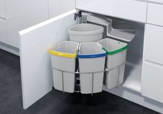 three trash cans in the corner of a kitchen cabinet with white cabinets and drawers behind them