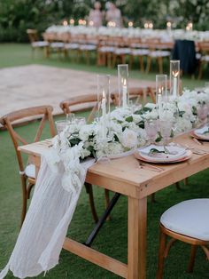 a long table with white flowers and candles on it is set for an outdoor dinner