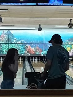 two people standing in front of bowling alleys and looking at an aquarium on the wall