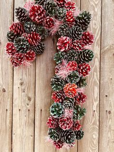 a wreath made out of pine cones on top of a wooden floor with red and green decorations