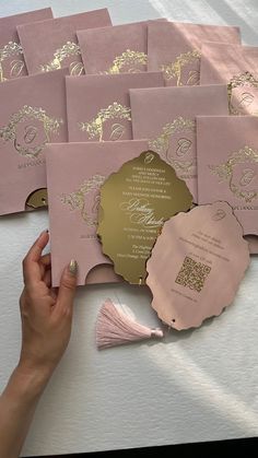 pink and gold wedding cards with tassels on the side, held up by a woman's hand