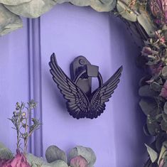 a purple door with a metal bird on it's side and flowers around it