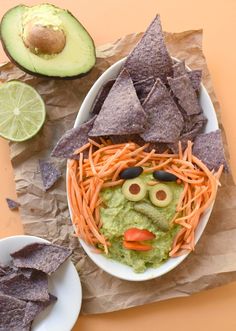 a bowl filled with guacamole, carrots and tortilla chips