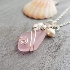 a pink sea glass necklace with two pearls on it and a seashell in the background