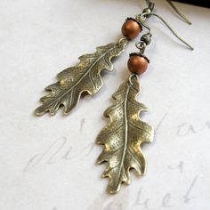 "Here is a lovely pair of oak leaf earrings, comprised of solid brass gold leaf charms, along with copper glass beads, which look like tiny acorns sitting atop the leaves. Earrings come on brass ear wires and are light weight and comfortable to wear. Adorable earrings, perfect for the nature lover! Made in the USA Oak keaf charms measure: 5/8\" x 1.5\" more from my collection here: http://www.etsy.com/shop/botanicalbird About: Botanical Bird is a collection of handcrafted fashion jewelry, both n Leaf Earrings Gold, Oak Leaf Earrings, Oak Leaf Necklace, Earrings Nature, Gold Bar Earrings, Earrings Fall, Gold Leaf Earrings, Fall Earrings, Leaf Jewelry