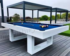 a pool table on a wooden deck with chairs and tables in the back ground behind it