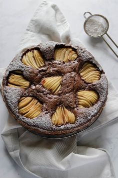 a chocolate cake with apples on top and powdered sugar around the edges, sitting on a white cloth