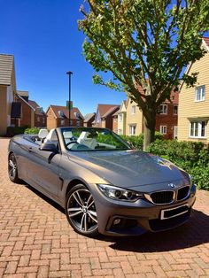 a silver bmw convertible parked on the side of a brick road in front of some houses