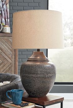 a table lamp sitting on top of a wooden table next to a blue cup and book