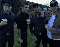 three men standing next to each other with drinks in their hands and one man wearing a hat