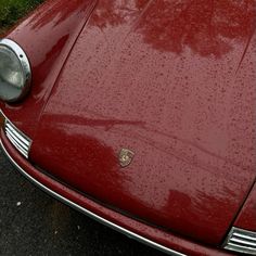 the front end of a red sports car with rain drops on it's hood