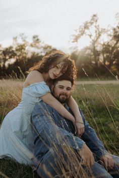 a man and woman are sitting in the grass with their arms around each other as they hug