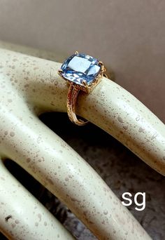 a gold ring with a blue topazte sits on a mannequin's dummy