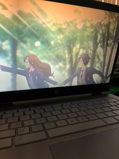 an open laptop computer sitting on top of a wooden table next to a window with anime characters