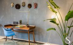 a blue chair sitting in front of a wooden desk next to a green plant and wall hangings