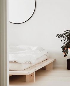 a white room with a bed, potted plant and round mirror on the wall