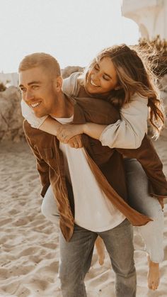 a man carrying a woman on his back at the beach in front of some sand