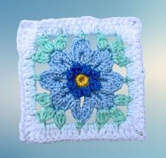 a crocheted square with a blue flower in the center and green leaves on it